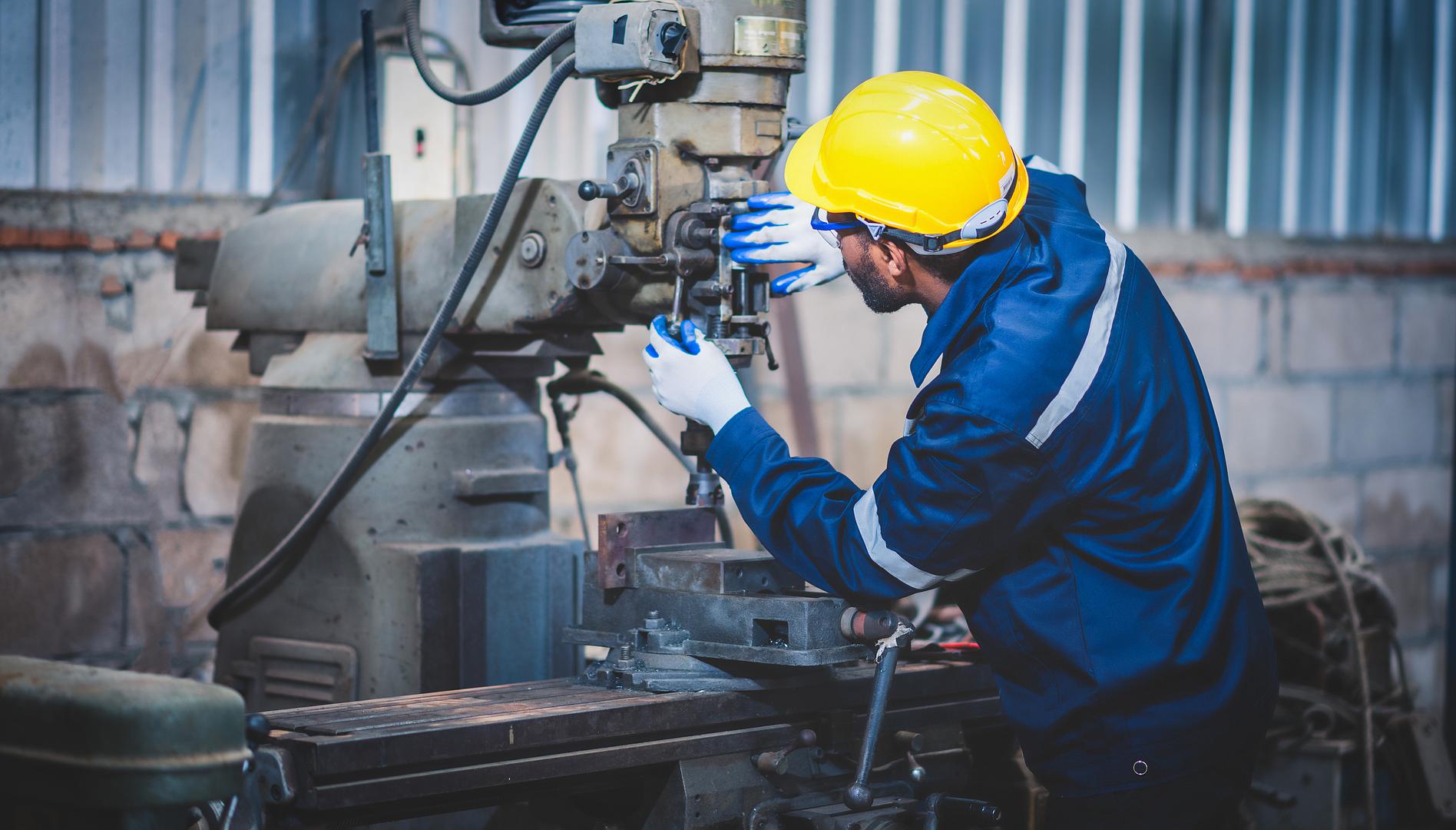 Technician in a hard hat repairing a milling machine