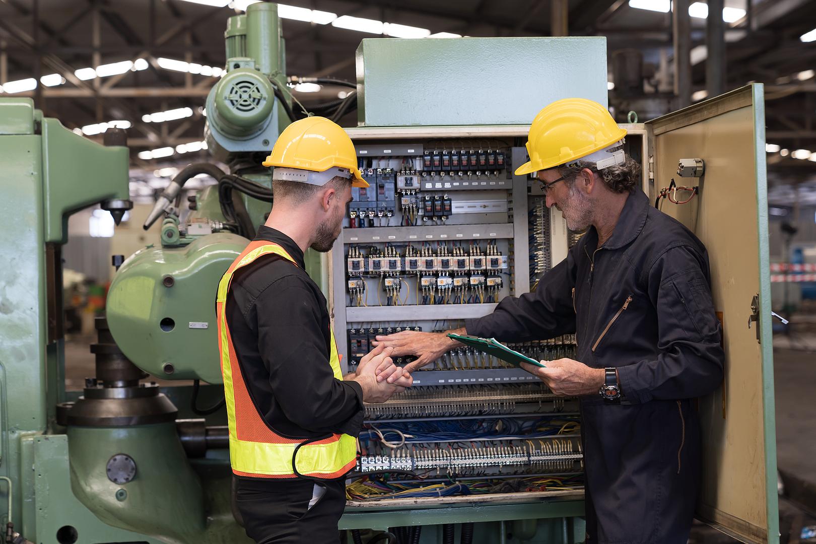 Two technicians reviewing an electrical cabinet on an industrial machine
